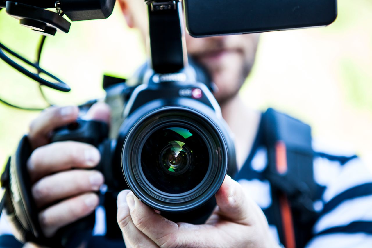 About A close-up shot of a cameraman filming, focusing on the camera lens and equipment.
